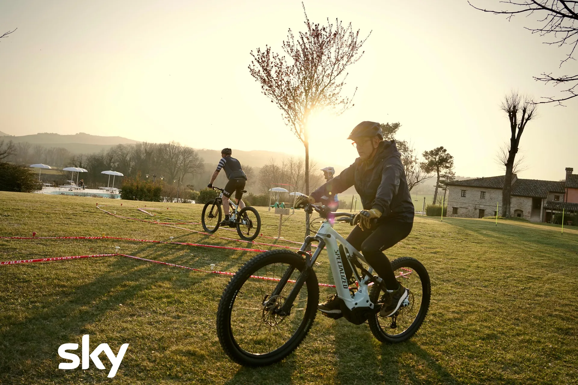 Bruno Barbieri in e-bike sul prato di Ca' Virginia al tramonto, il casale sullo sfondo