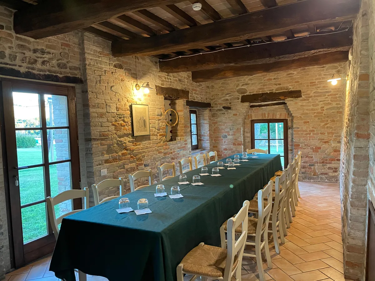 La sala della Locanda con pareti in pietra, travi a vista e la tavola apparecchiata verso il giardino