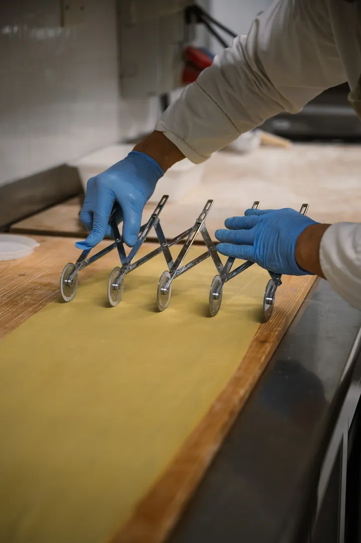 Mani che tagliano la sfoglia di pasta fresca sul tavolo di legno